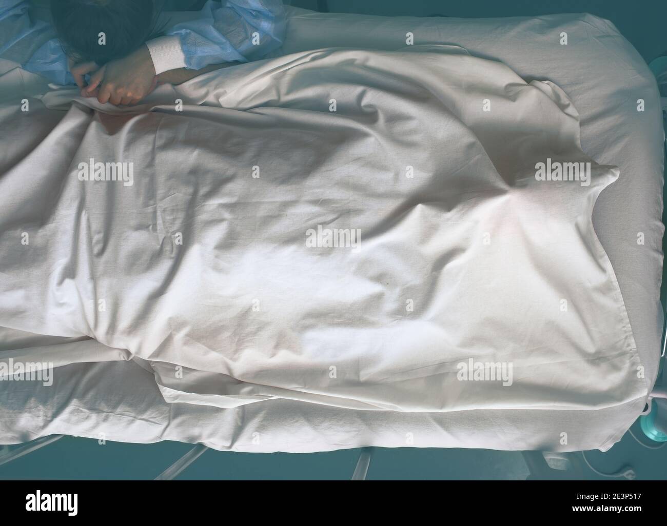 Young crying woman next to the deathbed of covered with bedsheet dead man. Stock Photo