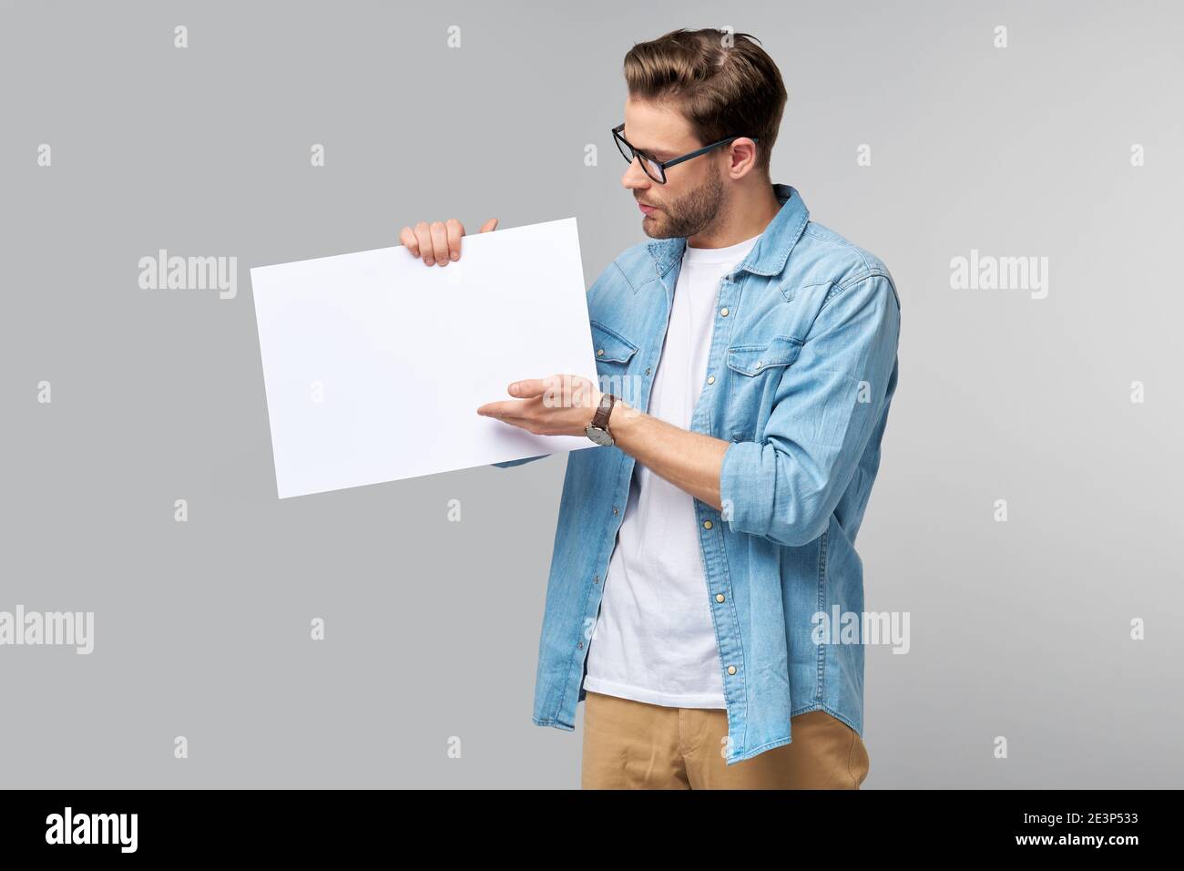 Portrait of a happy handsome young man holding blank white card or sign ...