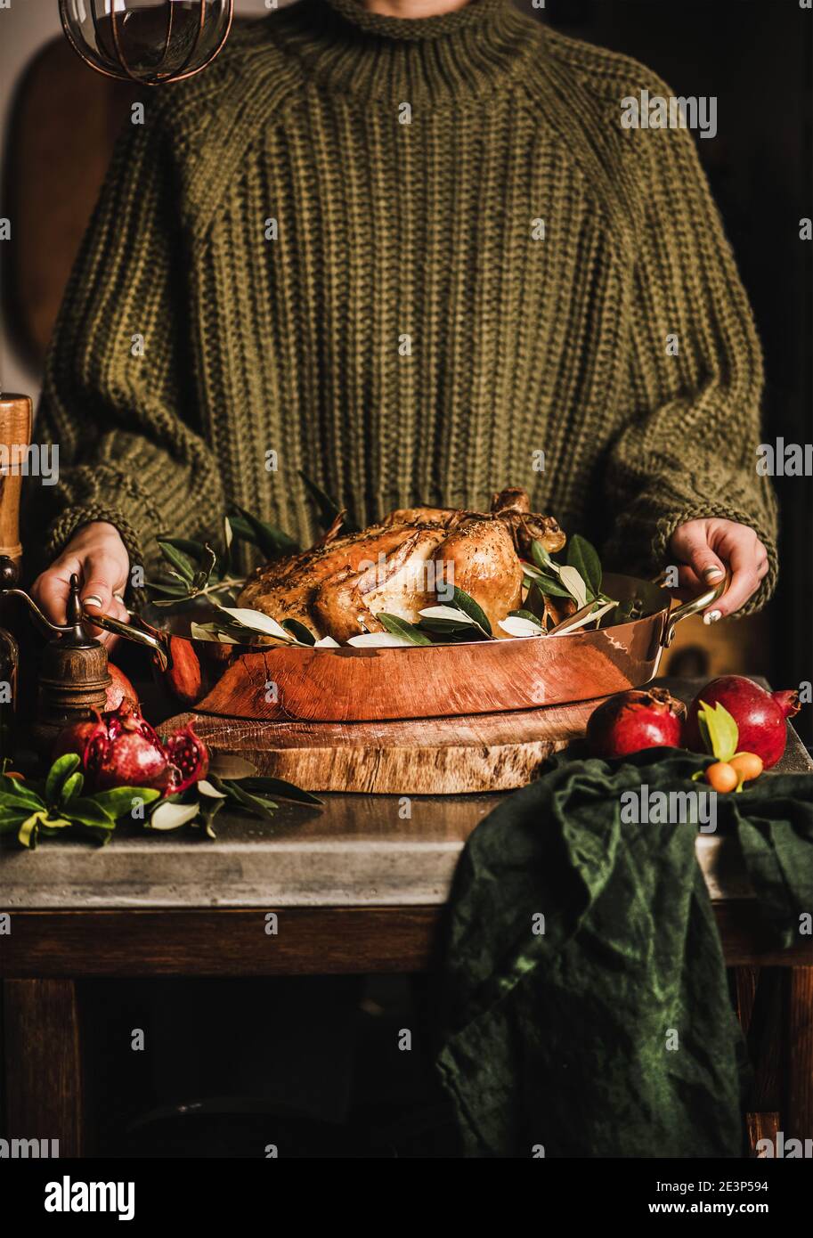 Female in knitted sweater holding whole roasted chicken for winter holiday festive dinner in copper roasting tin with spices, herbs and fresh fruit. Christmas or Thanksgiving Day cooking concept Stock Photo