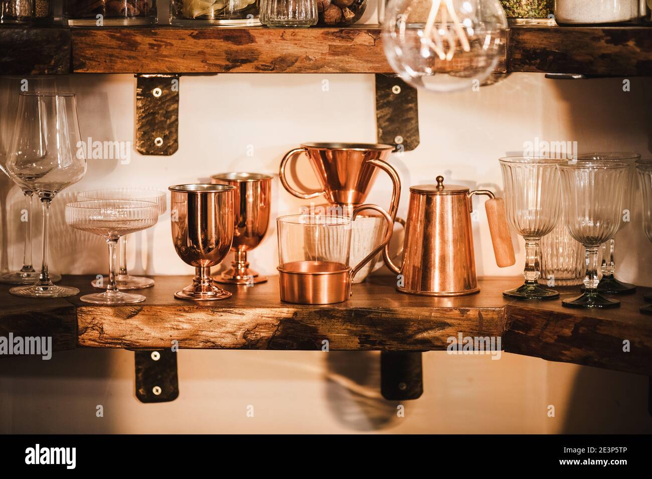 Kitchen shelves with various glass and copper glassware, mugs, tumblers and coffee utencils in beautiful daylight, horizontal composition. Interiors detail and lifestyle mood concept Stock Photo