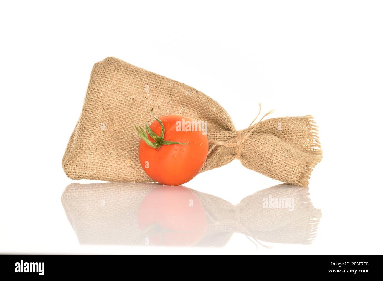 One whole red ripe juicy tomato with a green ponytail near a jute bag, on a white background. Stock Photo