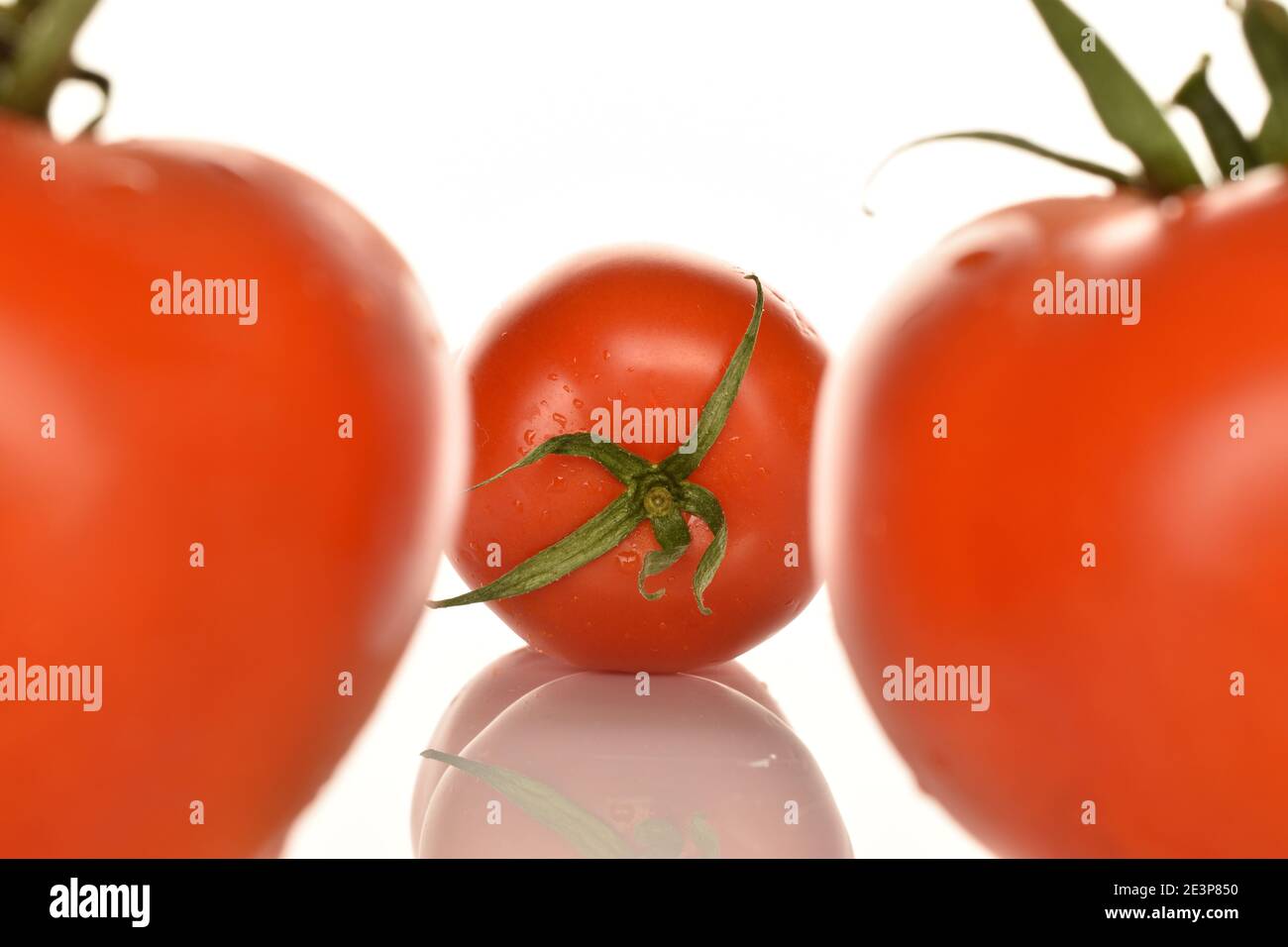In the center, in the background, in focus, is one whole red juicy tomato. Along the edges, in the foreground, out of focus, two parts of whole tomato Stock Photo