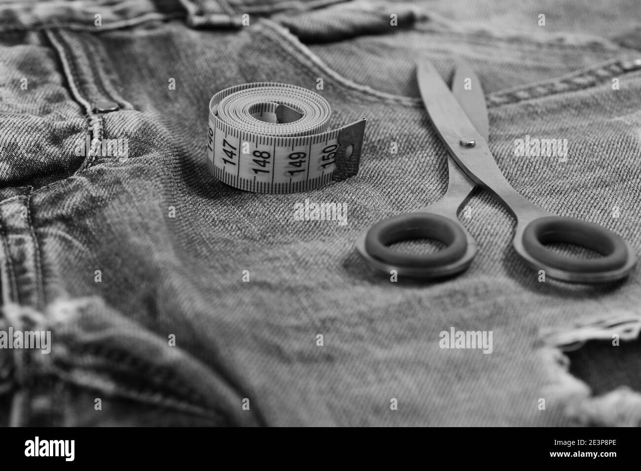 Tailors tools on denim fabric, selective focus. Making clothes and design concept. Jeans crotch and pocket, close up. Metal scissors and yellow measure tape on jeans. Stock Photo