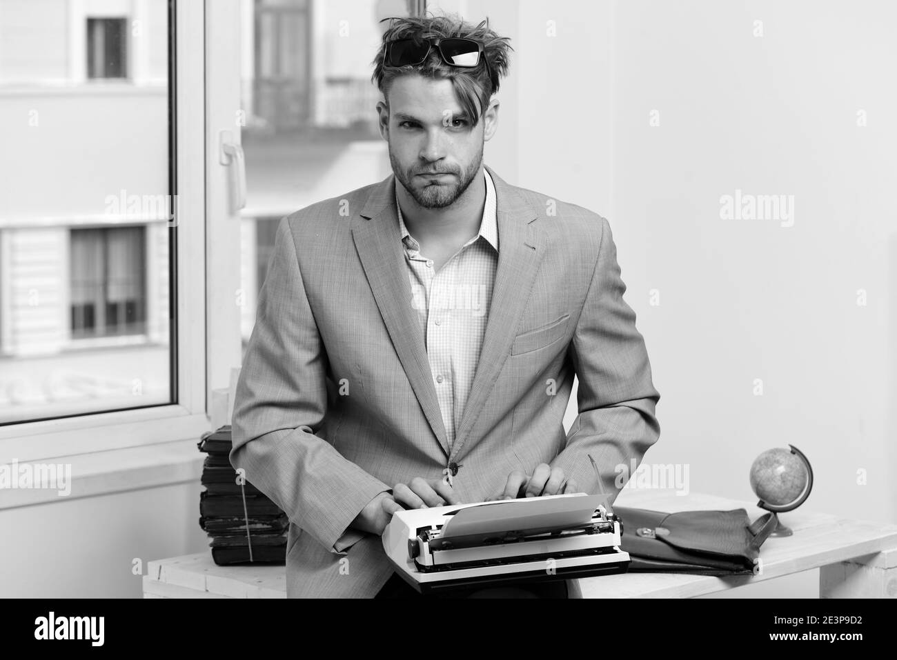Writer or businessman wearing grey suit. Man with serious face types story  or business report. Young author or editor writes story on old typewriter  on window background. Editing and writing concept Stock