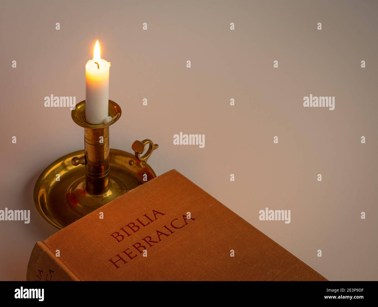 a candle on a stick shining with soft ligt on a hebrew bible on a white