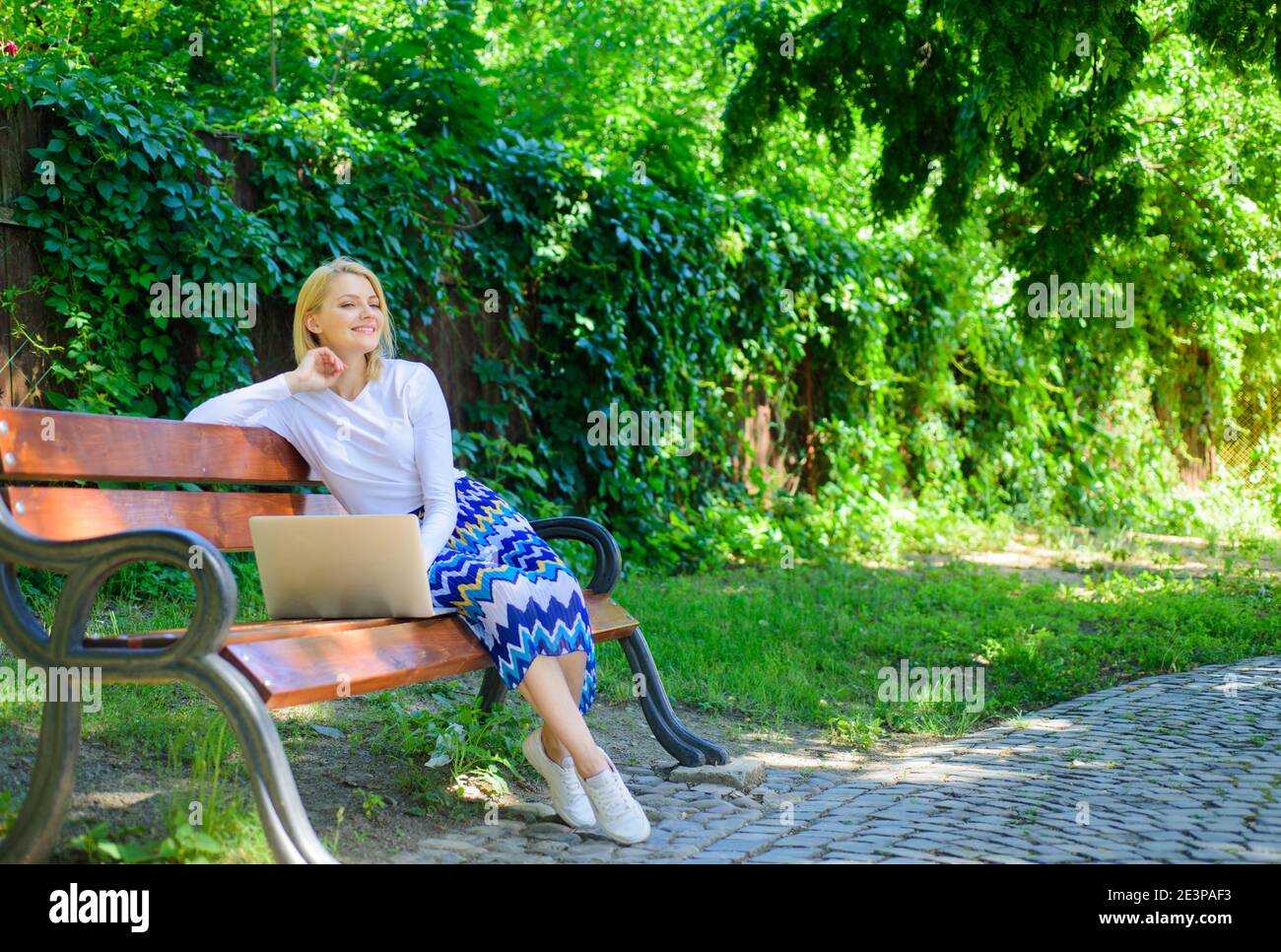 Save your time with shopping online. Shopping online. Girl sit bench with notebook. Woman with laptop in park enjoy green nature and fresh air. Girl dreamy takes advantage of online shopping. Stock Photo