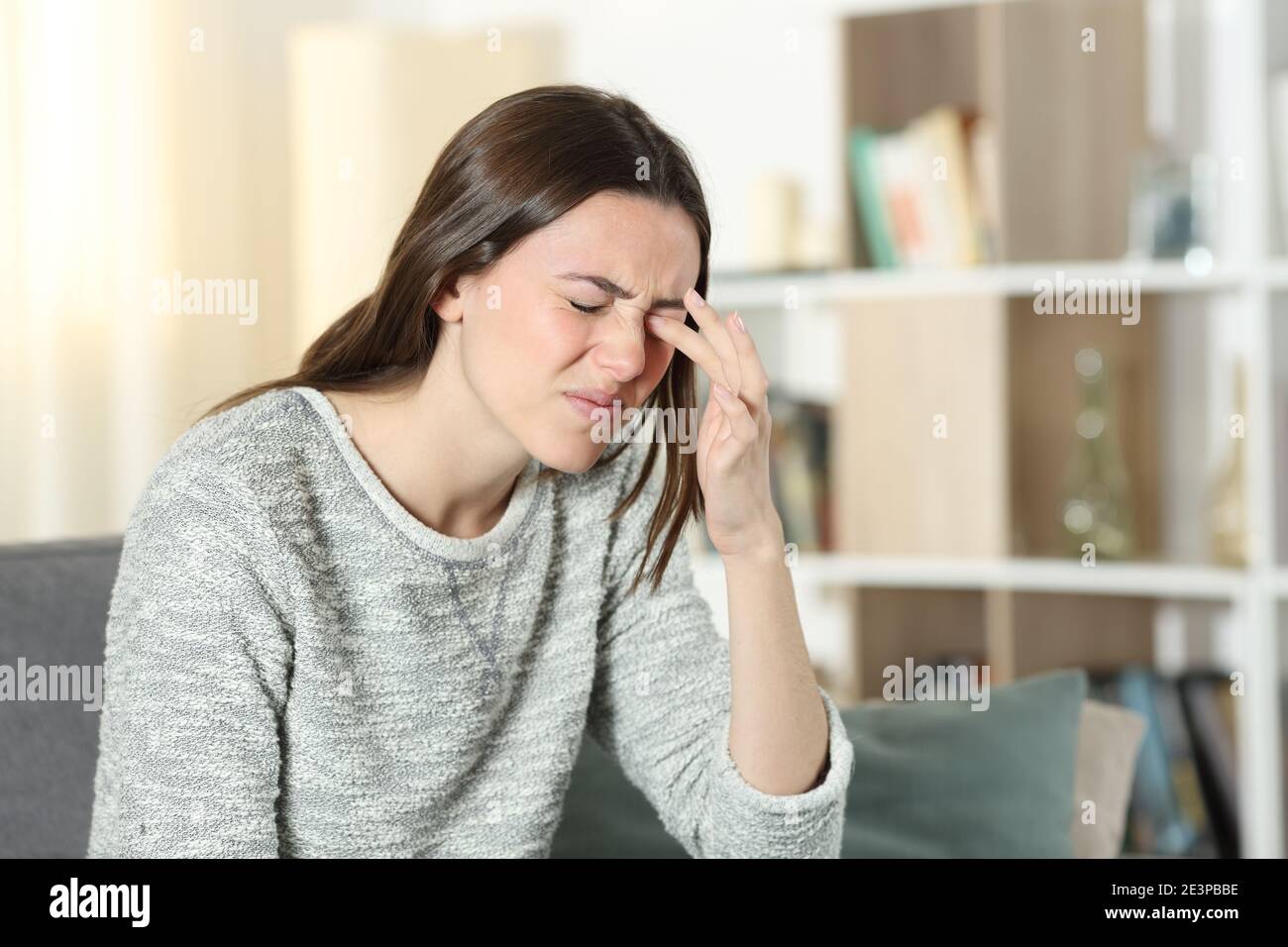 Woman scratching itchy eye sitting on a couch at home Stock Photo