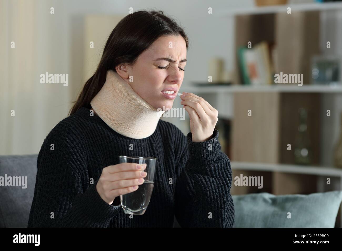 Disabled woman with ache taking pill complaining sitting on a couch at home Stock Photo