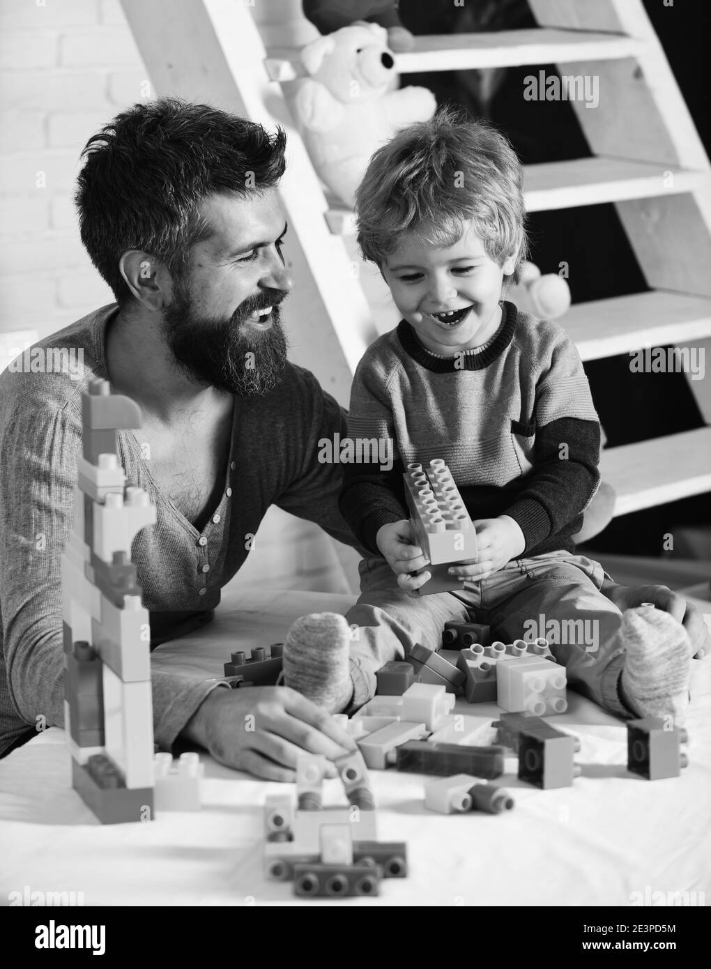 Dad and kid with ladder on background build of plastic blocks. Family and childhood concept. Man and boy play together. Father and son with happy faces create colorful constructions with toy bricks. Stock Photo