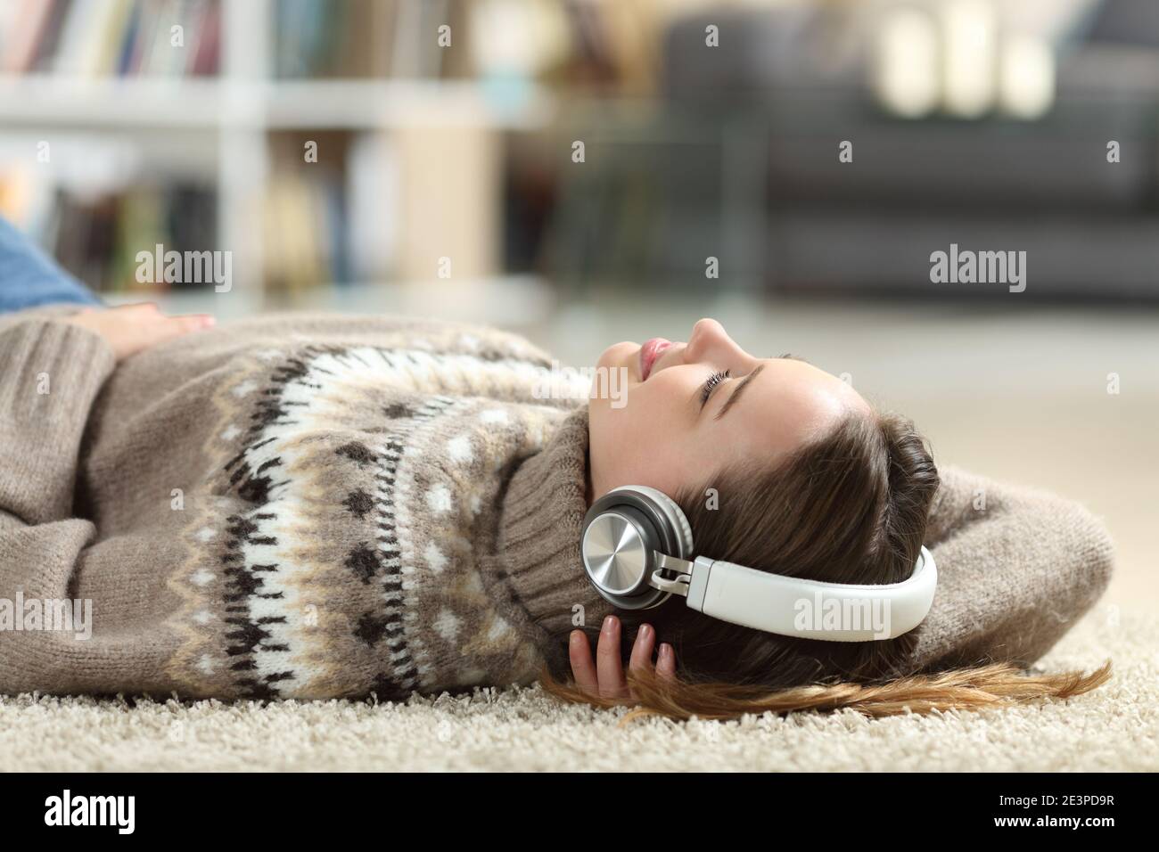 Relaxed teen listening to music wearing headphones lying at home in winter Stock Photo