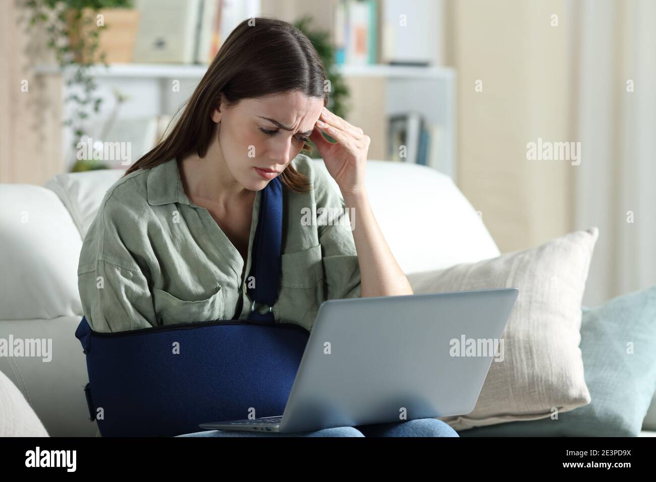 Worried handicapped woman reading bad news on laptop sitting on a couch in the living room at home Stock Photo