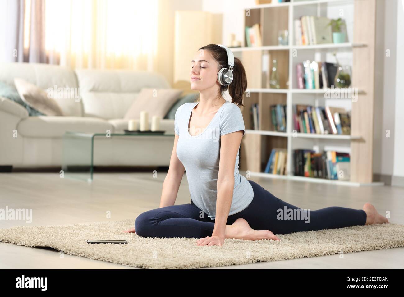 Concentrated woman doing yoga exercise listening audio tutorial with headphones at home Stock Photo