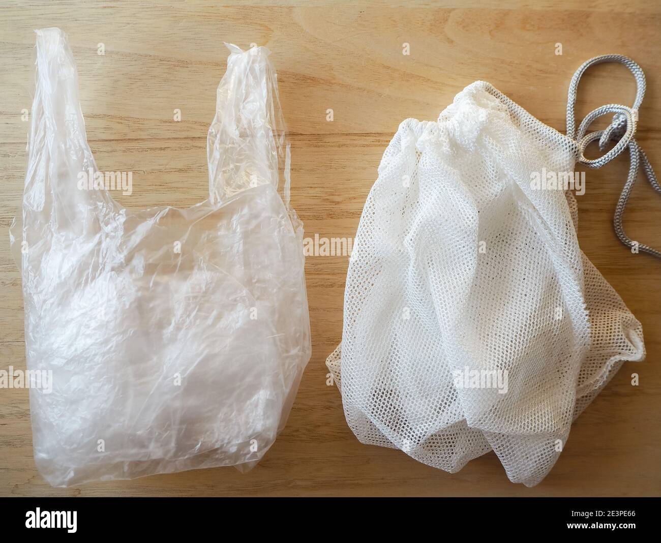 Single-use plastic bag and reusable vegetable bag as a sustainable solution on a wooden background. EU single-use plastic ban concept. Stock Photo