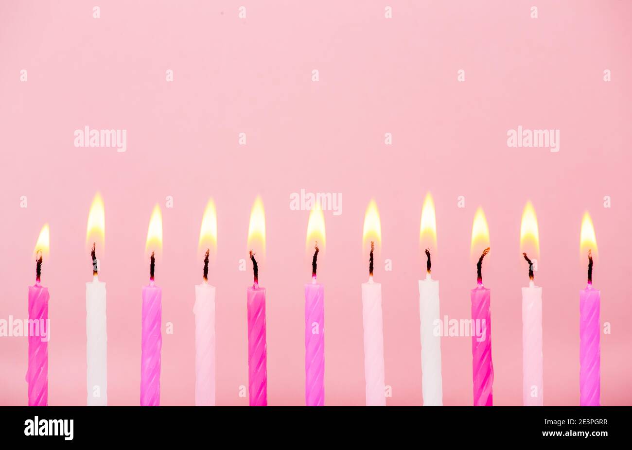 Various pink color birthday cake candles burning in line on pastel pink background, studio shot, lot of copy space for greetings. Side view. Stock Photo