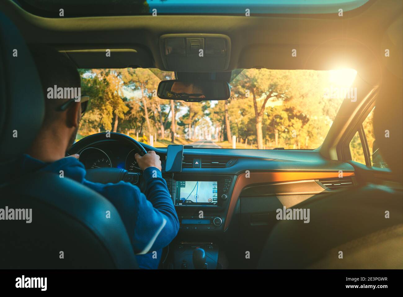 Young man driving car at sunset. Man using navigation system while driving a car Stock Photo