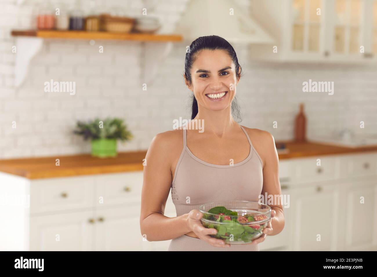 Portrait of slim woman in sports top holding bowl of vegetable salad and smiling at camera Stock Photo
