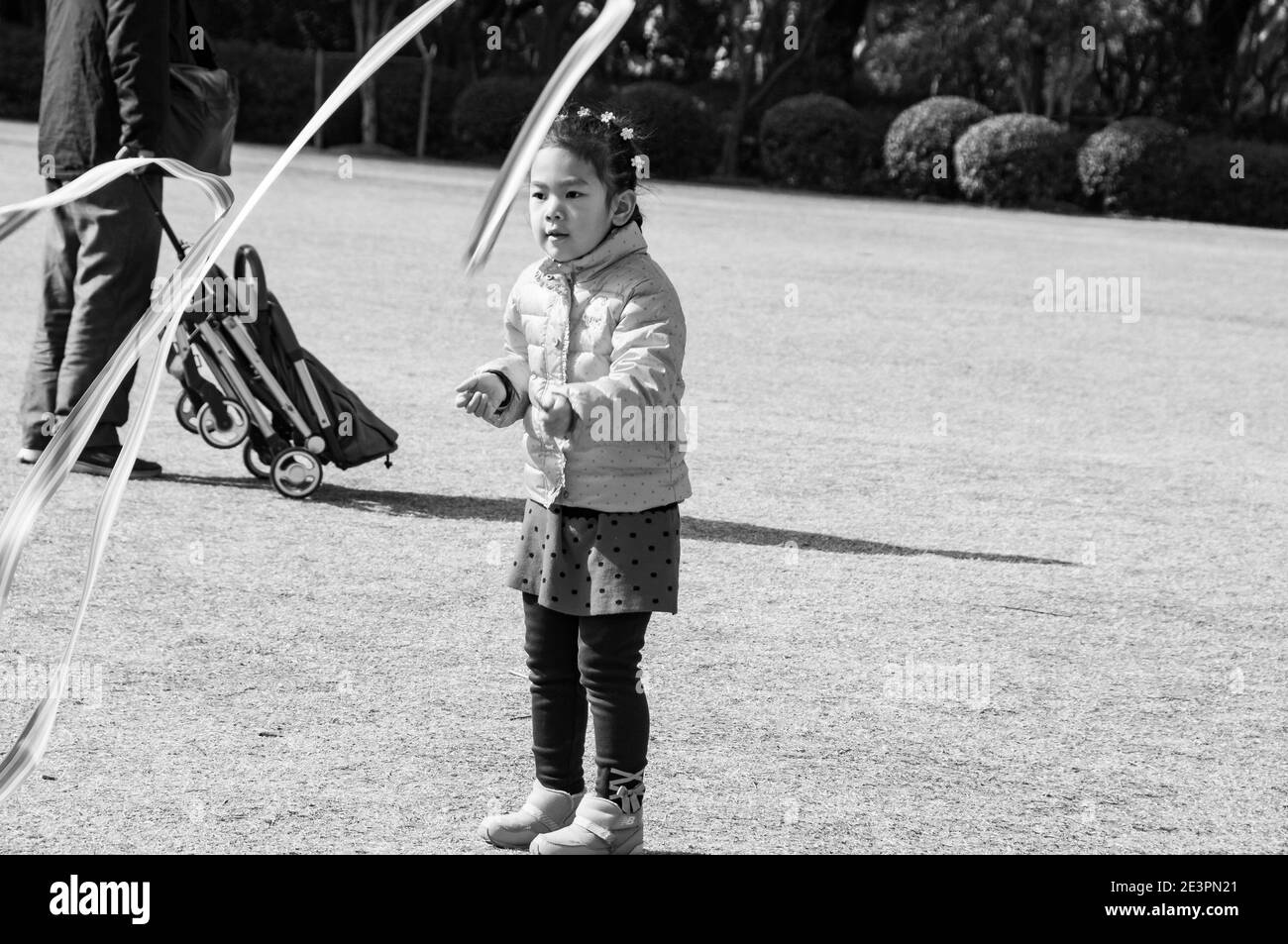 A young girl plays with a ribbon on a stick in Shanghai’s Fuxing Park. Stock Photo