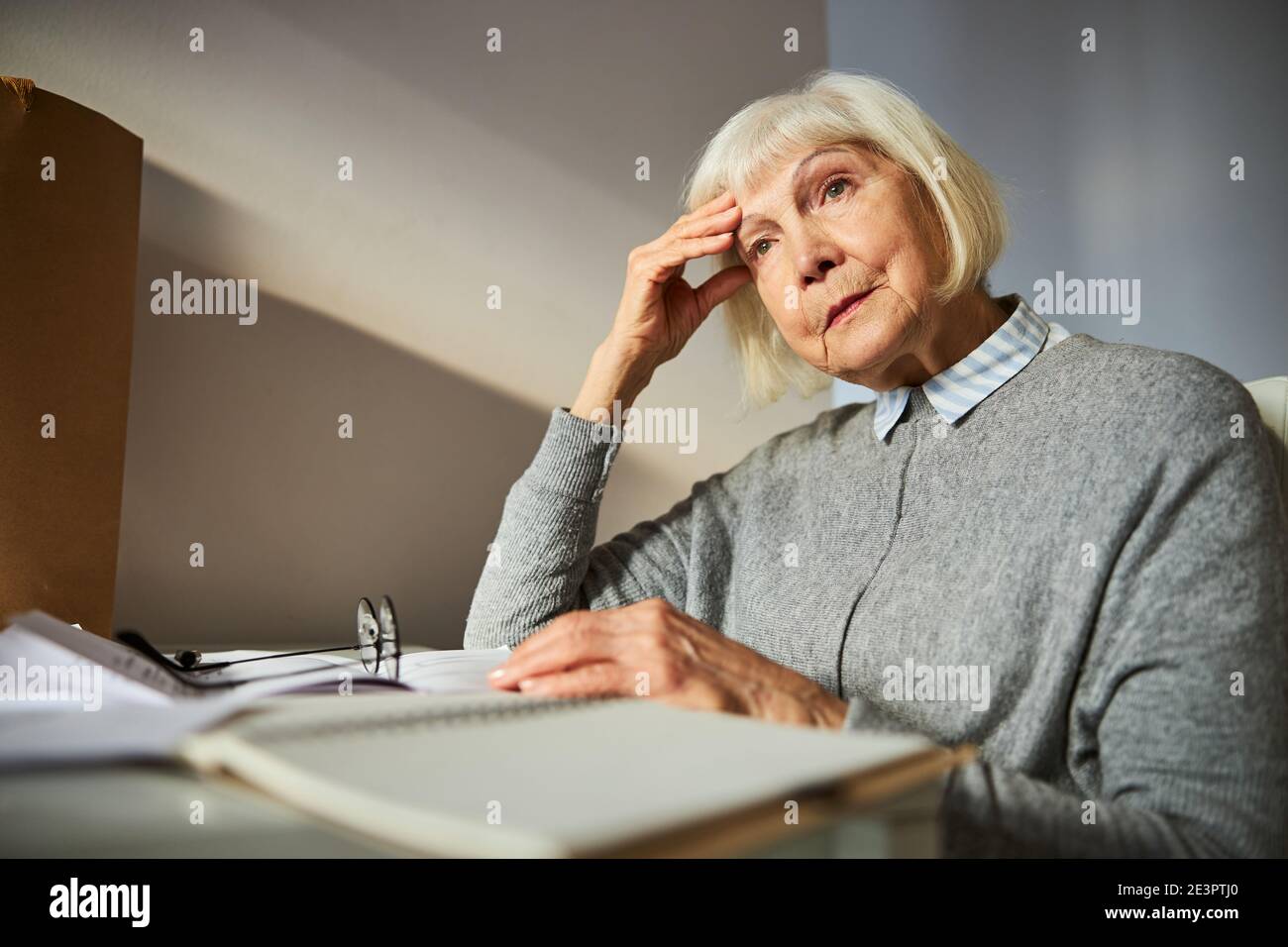 Sad aged woman sitting at the desk Stock Photo