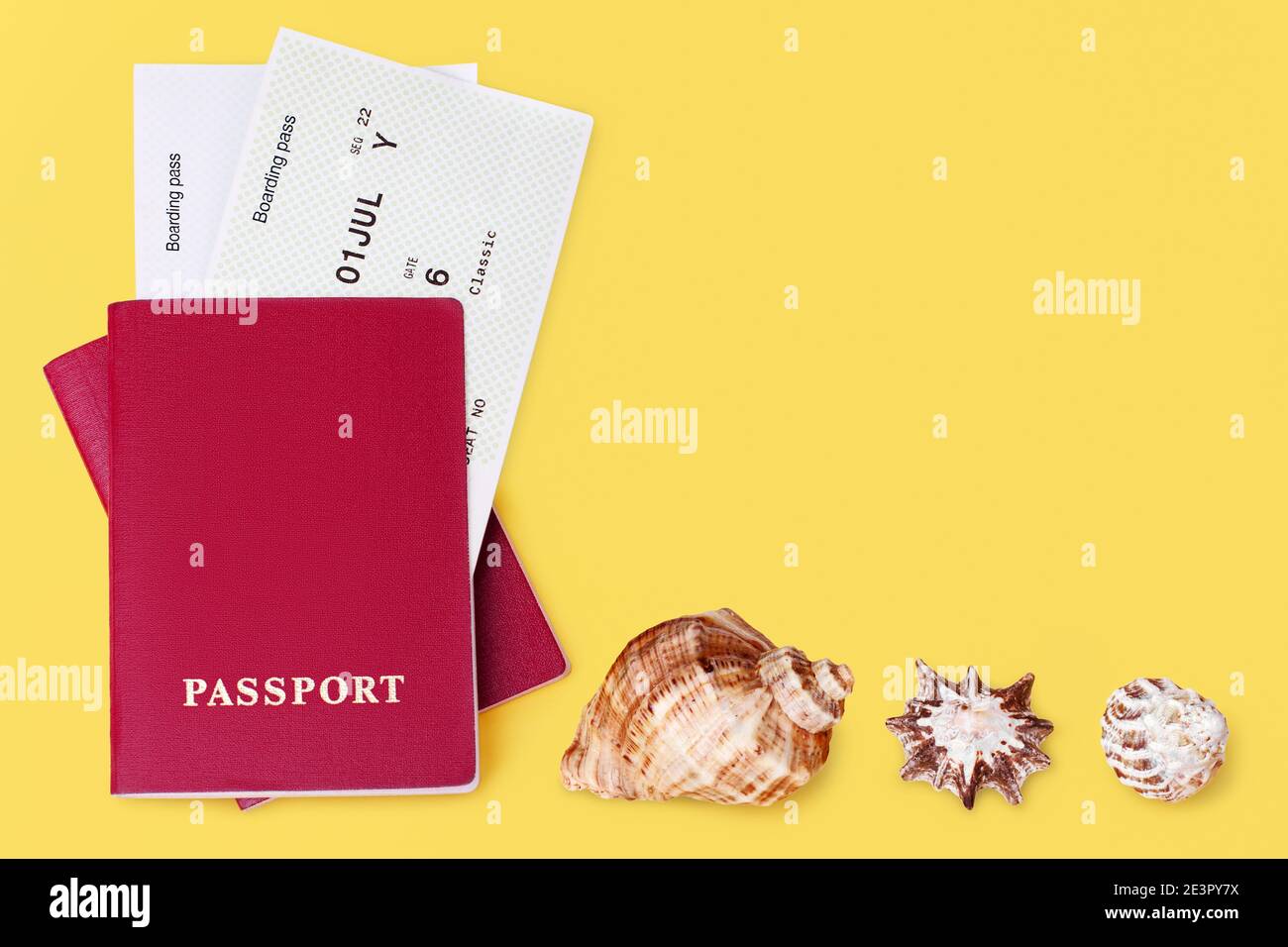 Red passport, boarding pass, seashells yellow background closeup top