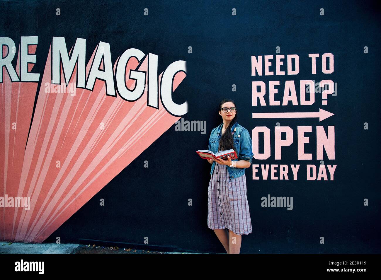 USA / New York City /Young woman reading a book in fron of the wall art outside of  Indie bookstore 'Books Are Magic' in Brooklyn , New York Stock Photo