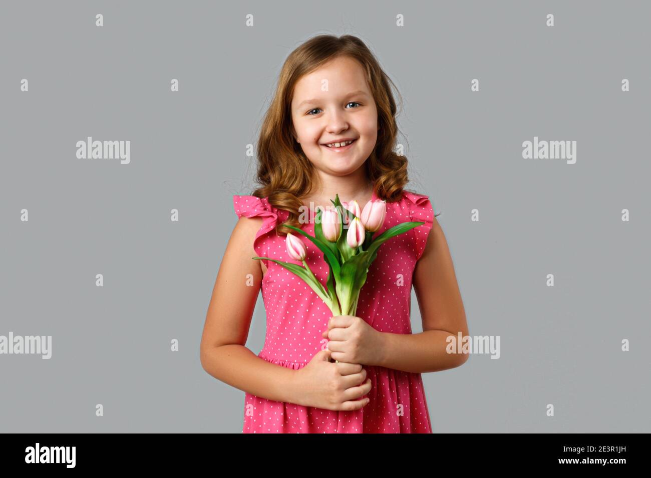 Cute happy little girl in a pink dress with polka dots on a gray ...