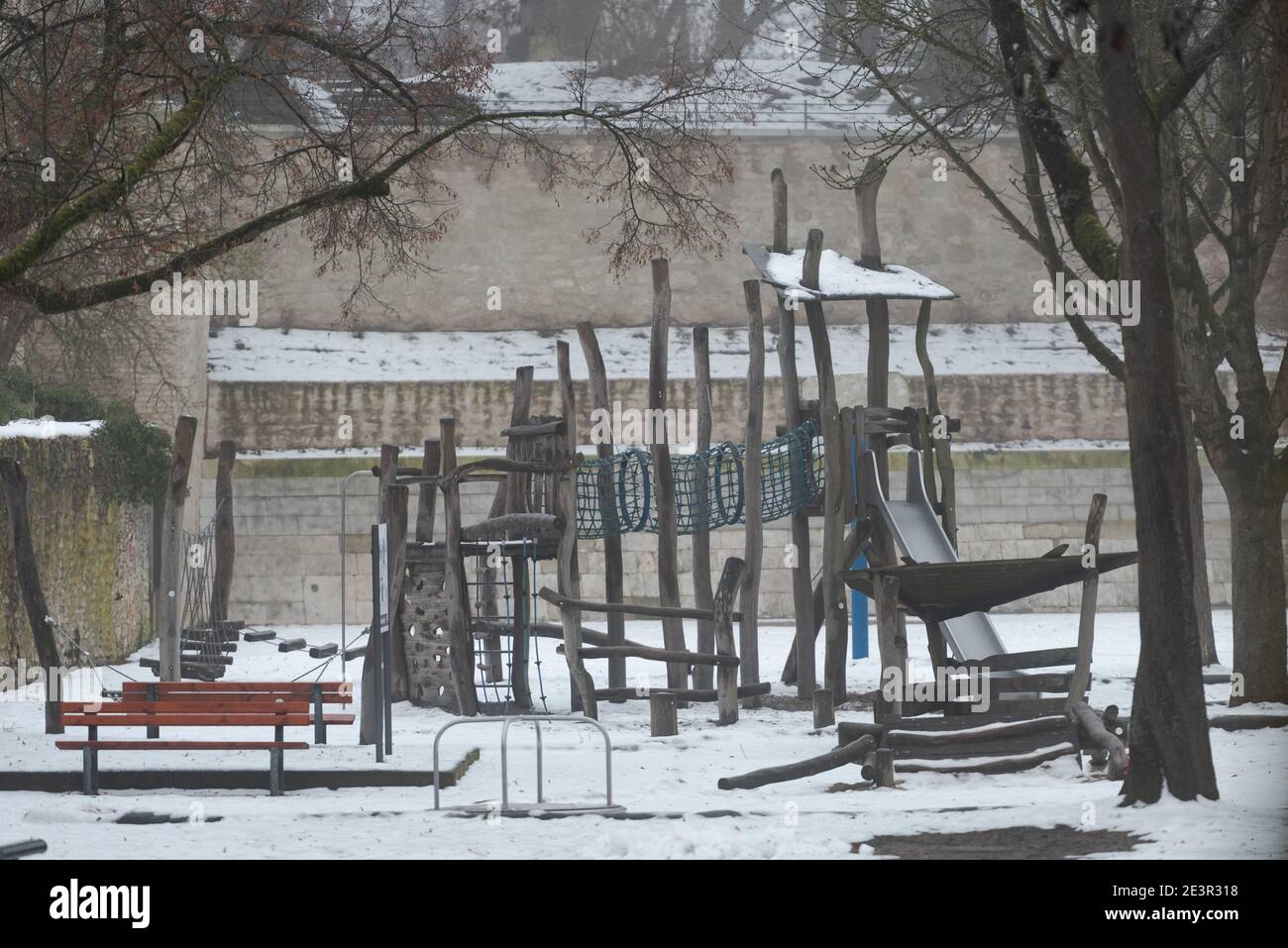 Snow covered deserted children´s playground with slide and climbing towers surrounded by stone buildings and walls in the old town of Regensburg in wi Stock Photo