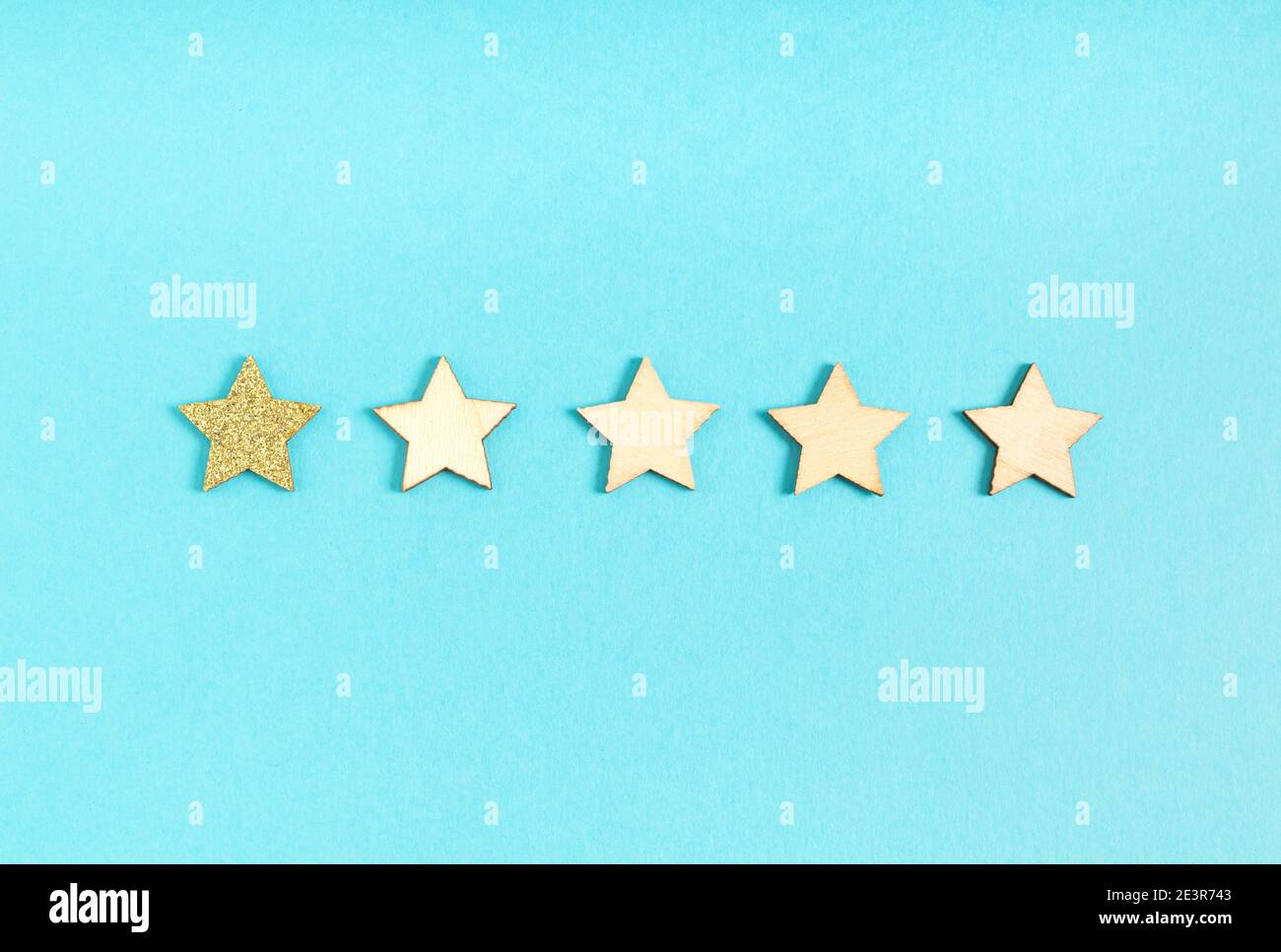 One star rating, one gold glittery star and four wooden stars on a blue background Stock Photo