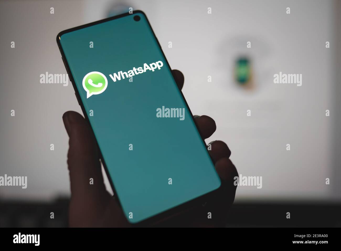 Man holding a smartphone with Whatsapp messenger app logo displayed on the screen in front of the Whatsapp web version Stock Photo