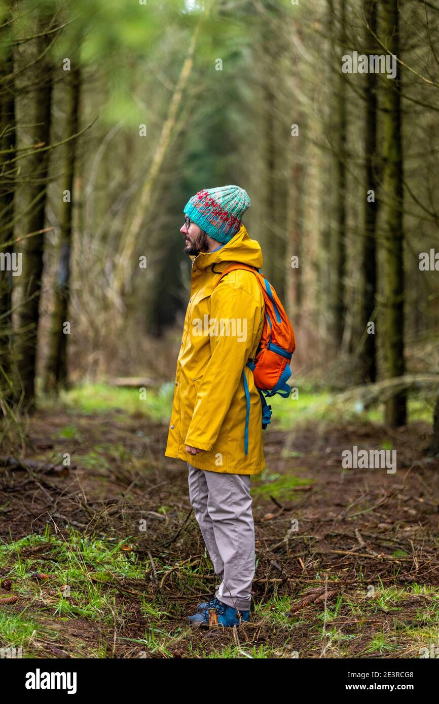 Man wearing yellow raincoat and backpack standing in forest Stock Photo