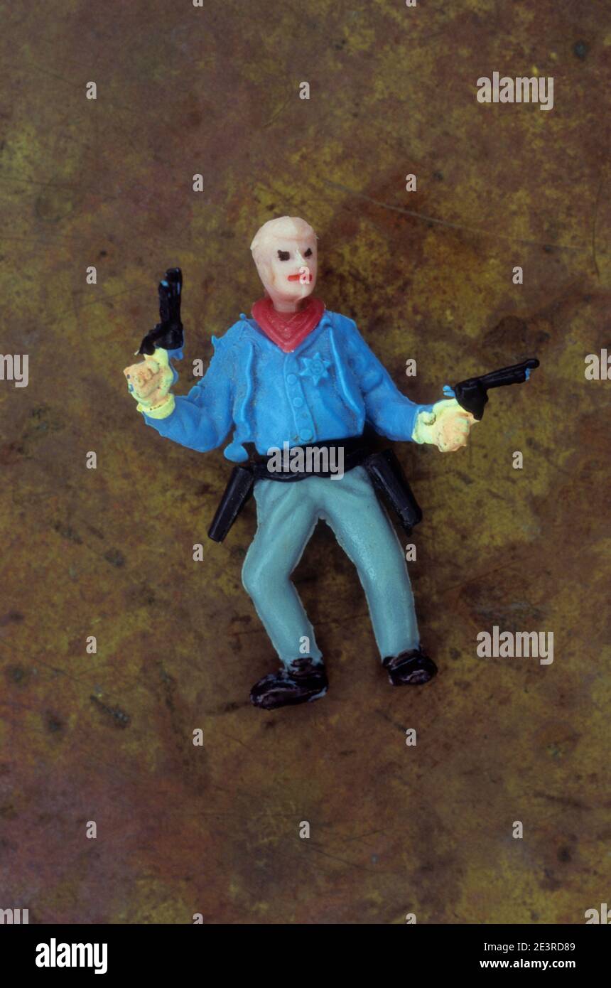Plastic model of cowboy with no hat and prominent red lips standing with guns in both hands Stock Photo
