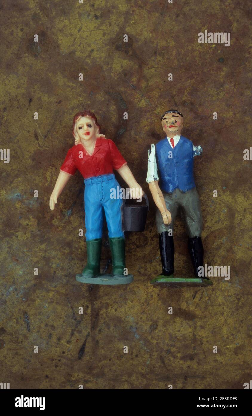 Plastic model of female farm or stable worker carrying bucket and standing next to male worker with missing arm Stock Photo