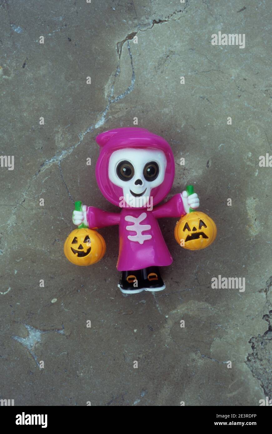 Plastic model of joke human skeleton with smiling skull wearing pink hooded cloak and holding carved pumpkins Stock Photo