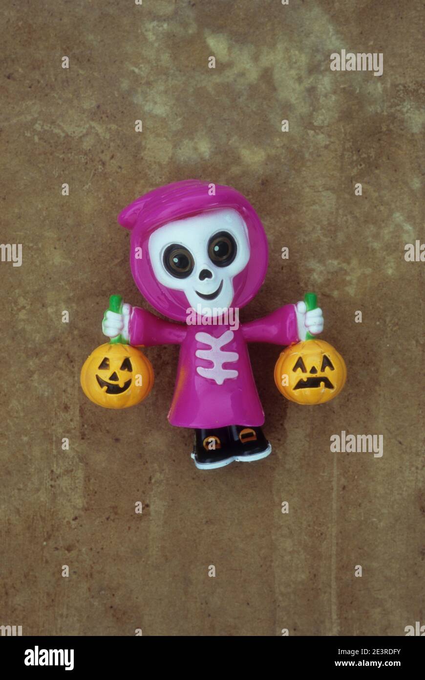 Plastic model of joke human skeleton with smiling skull wearing pink hooded cloak and holding carved pumpkins Stock Photo