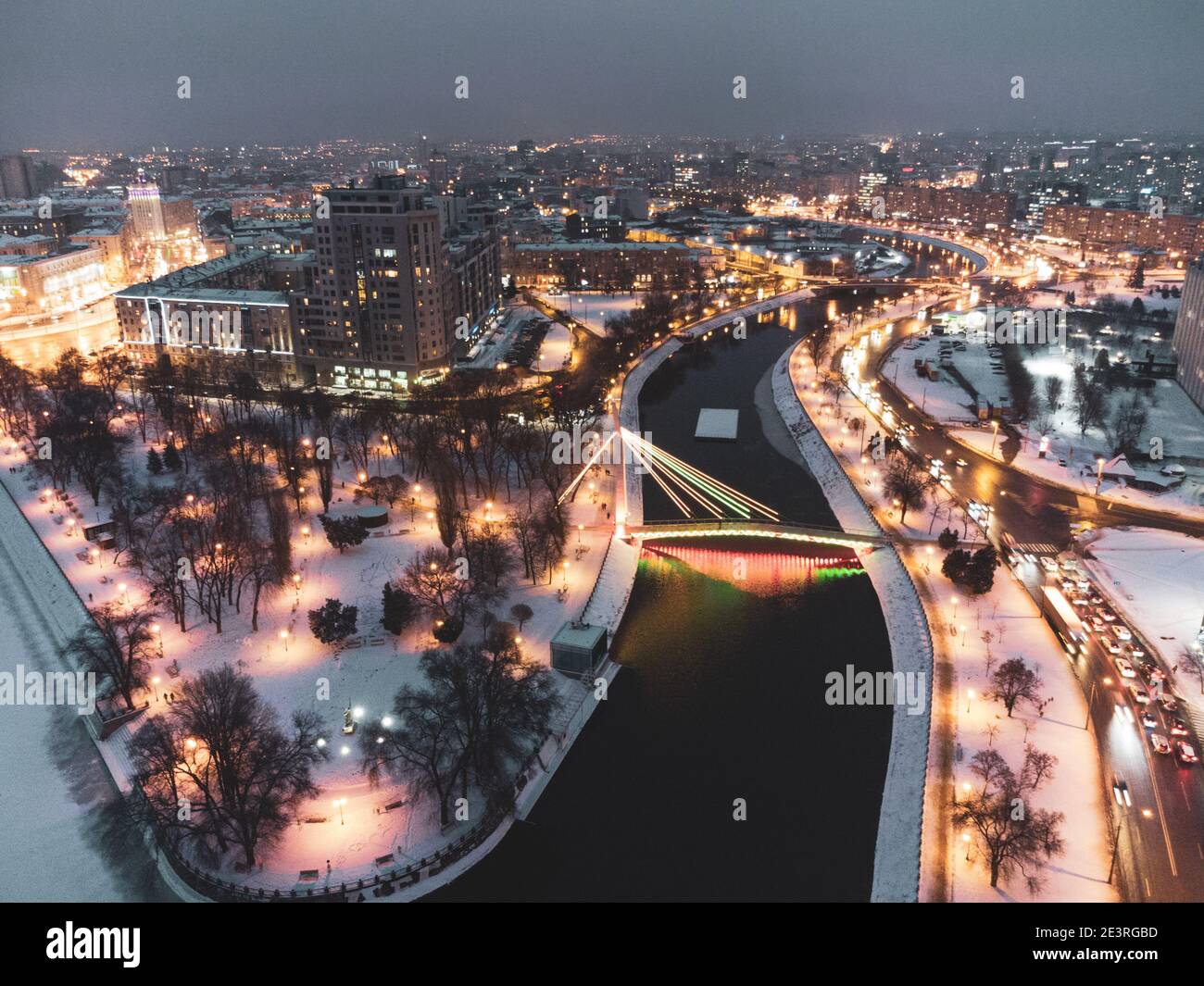 Bridge (Mist Zakokhanykh) across river in illuminated Skver Strilka in Kharkiv city center. Winter aerial evening color graded cityscape photography Stock Photo
