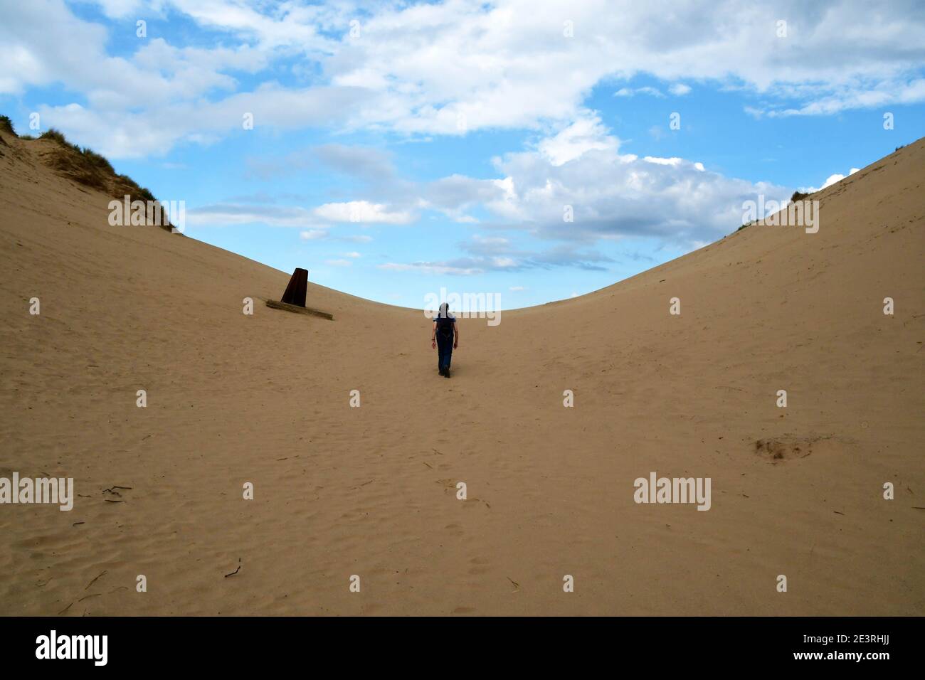 Walker climbs the large sand dunes past a sunken marker at Braunton Burrows in Devon on a hot sunny day.UK Stock Photo
