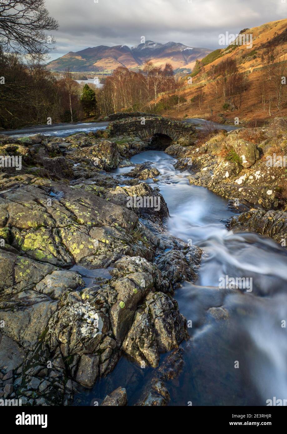 Barrow Beck tumbles down the Ashness Fells towards Derwent Water under Ashness Bridge, with the Skiddaw Massif visible on the horizon. Stock Photo
