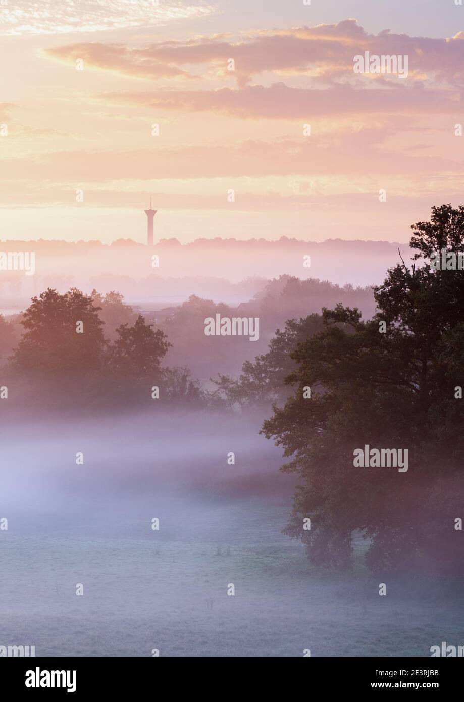 A pastel sunrise in the Poitou-Charentes countryside near Confolens creates beautiful layers in the misty landscape with a water tower on the horizon. Stock Photo