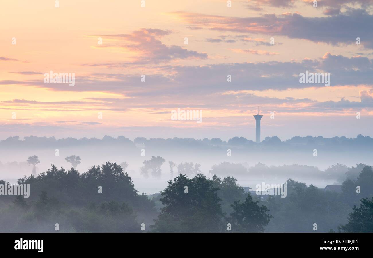 A pastel sunrise in the Poitou-Charentes countryside near Confolens creates beautiful layers in the misty landscape with a water tower on the horizon. Stock Photo