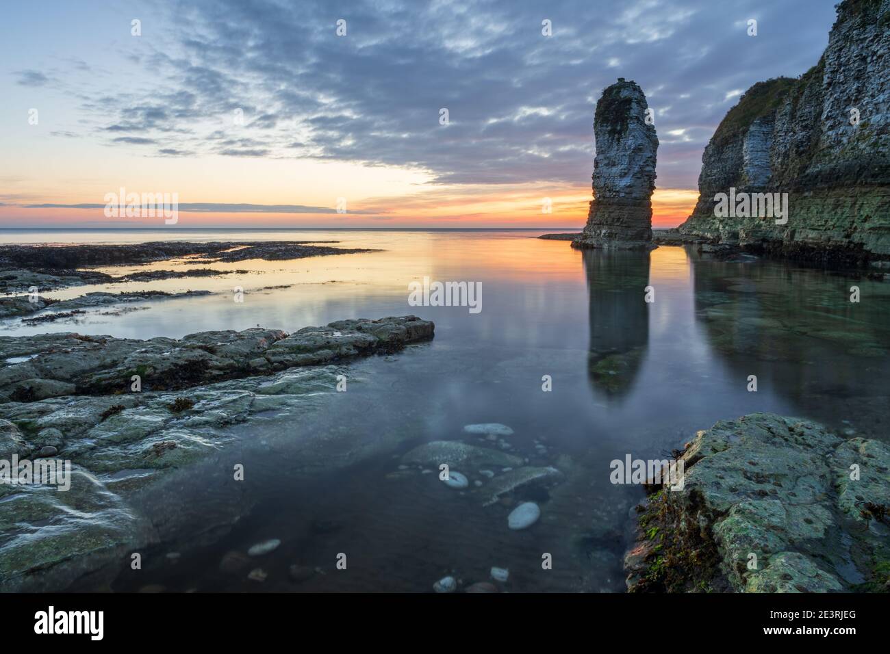 The first glow of sunrise highlights the bank of cloud behind the prominent sea stack at Selwicks Bay on the Yorkshire coast. Stock Photo