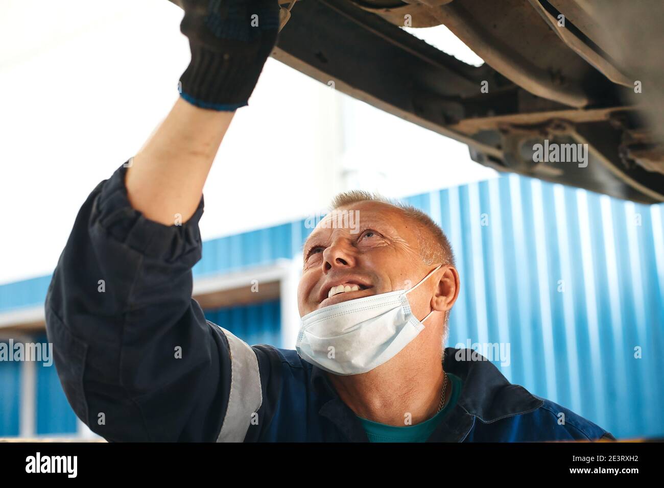 A car mechanic in a medical mask smiles and repairs the car. An attentive  car mechanic does the job Stock Photo - Alamy