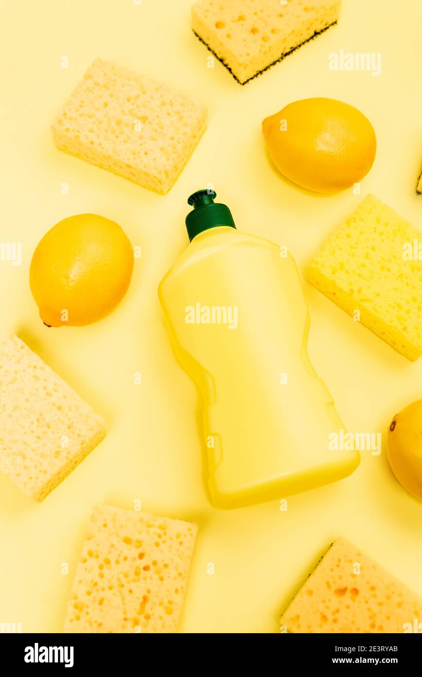 Top view of dishwashing liquid, sponges and lemons on yellow background