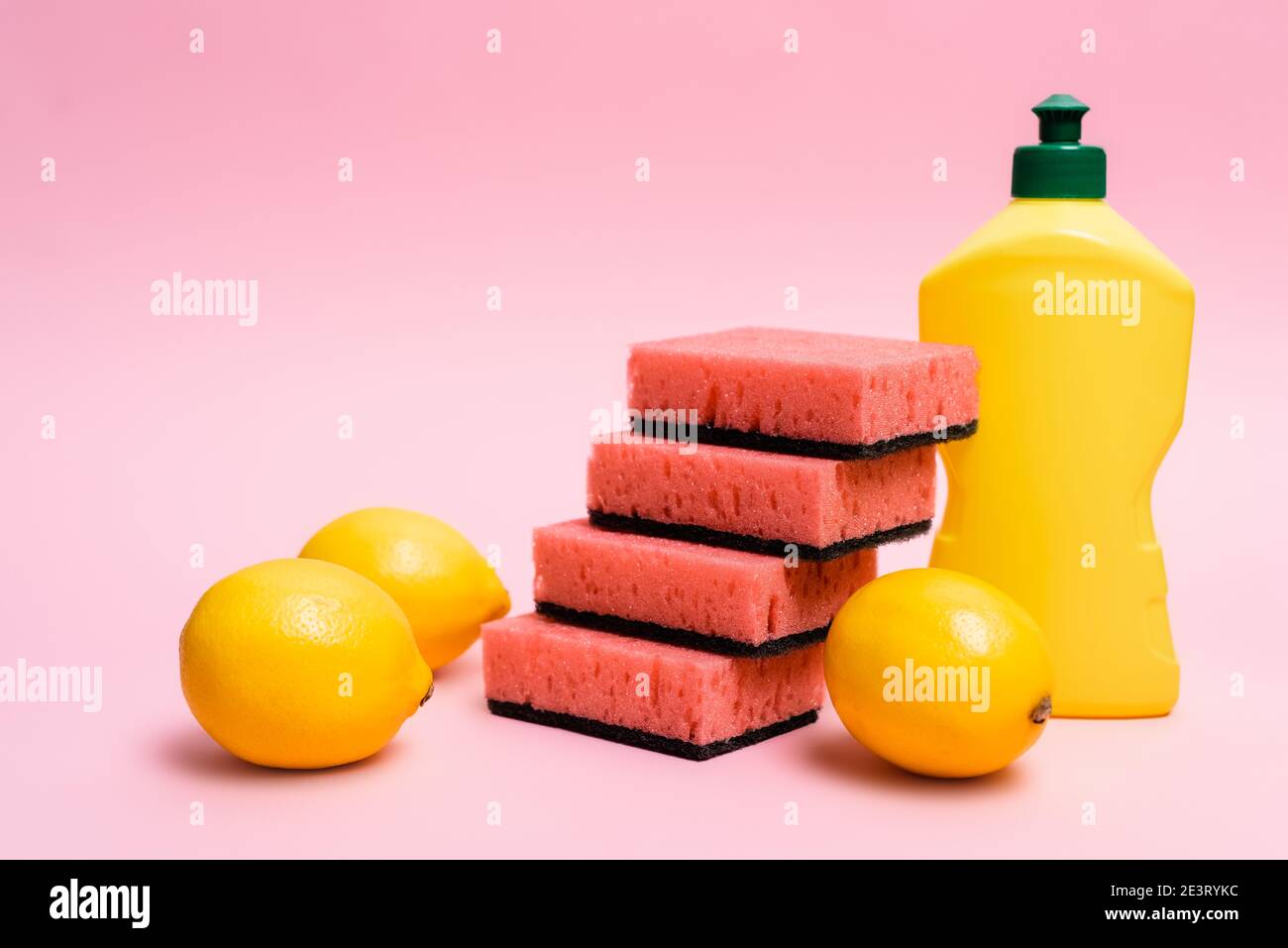 Fresh lemons near sponges and dishwashing liquid on pink background