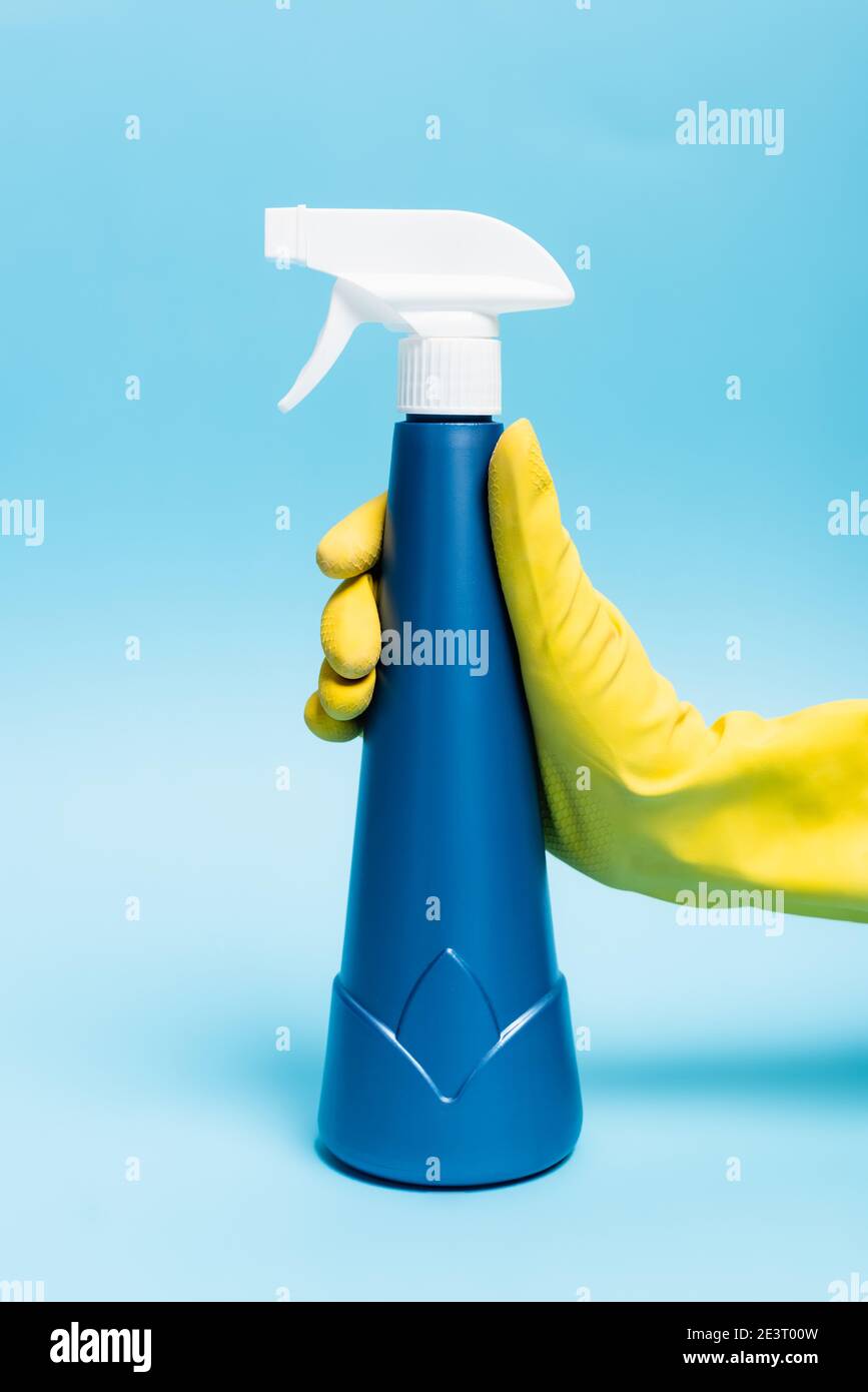 Hand in yellow rubber gloves holding detergent with sprayer on blue ...