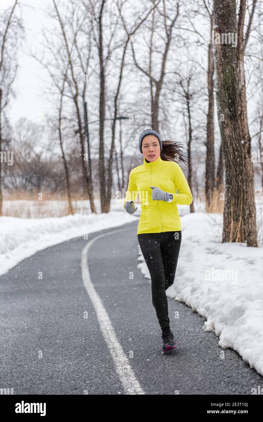 Winter runner girl training running in snow wearing cold weather clothes gloves warm yellow jacket. Asian woman jogging in park during snowfall Stock Photo Alamy