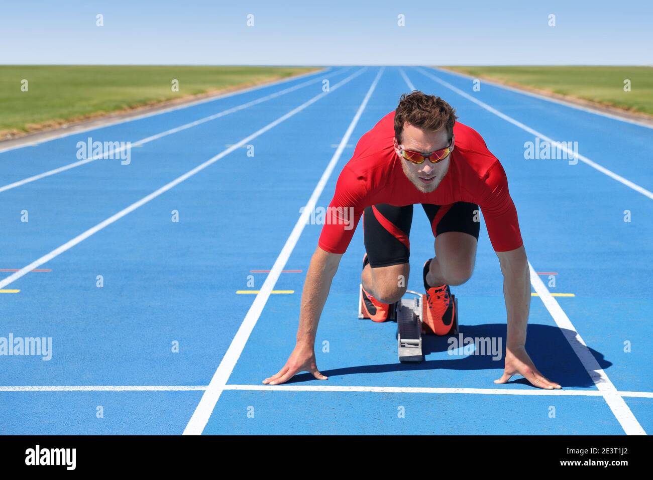 Starting to run athlete sprinter ready to run on blue tracks in track and field event race at start line at outdoor stadium. Focus and motivation Stock Photo