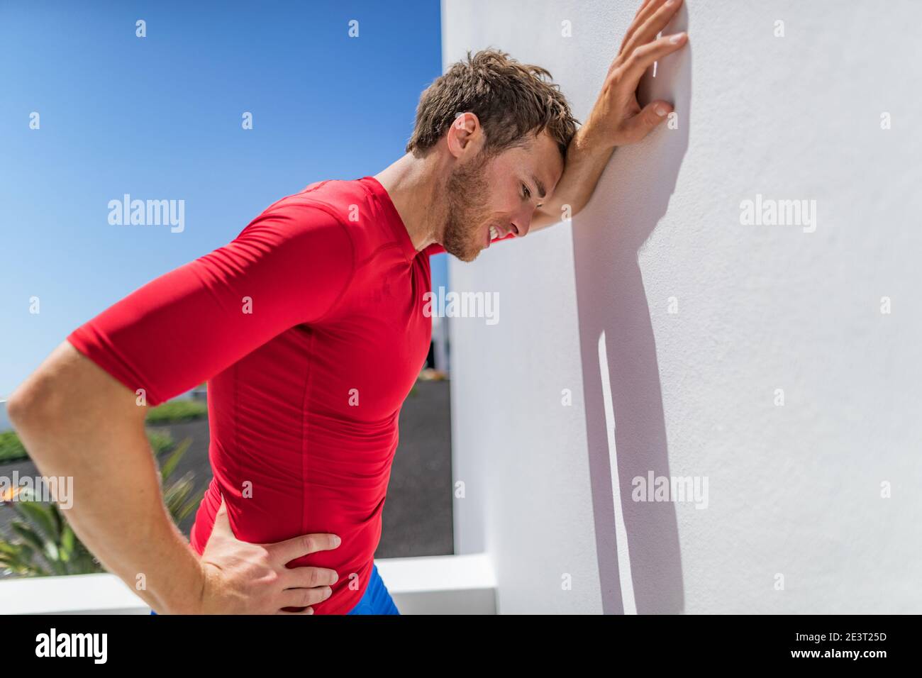 Tired athlete runner man exhausted leaning on wall of fatigue breathing