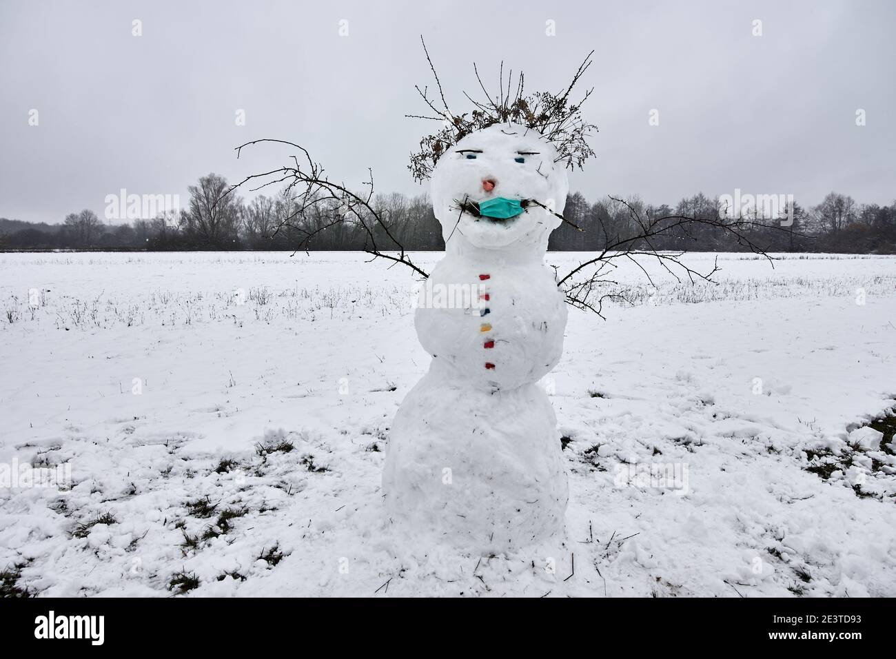 Funny snowman on snowy field wearing a medical face mask against coronavirus, Covid-19 Stock Photo