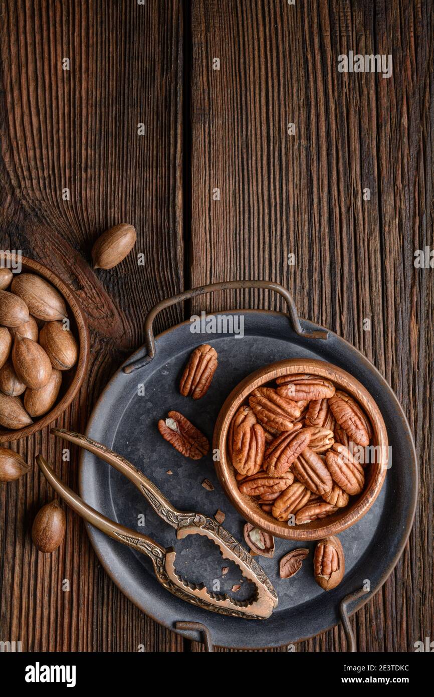 Healthy snack rich in vitamins and minerals, fresh shelled and in-shell pecans in a bowl on wooden background with copy space Stock Photo