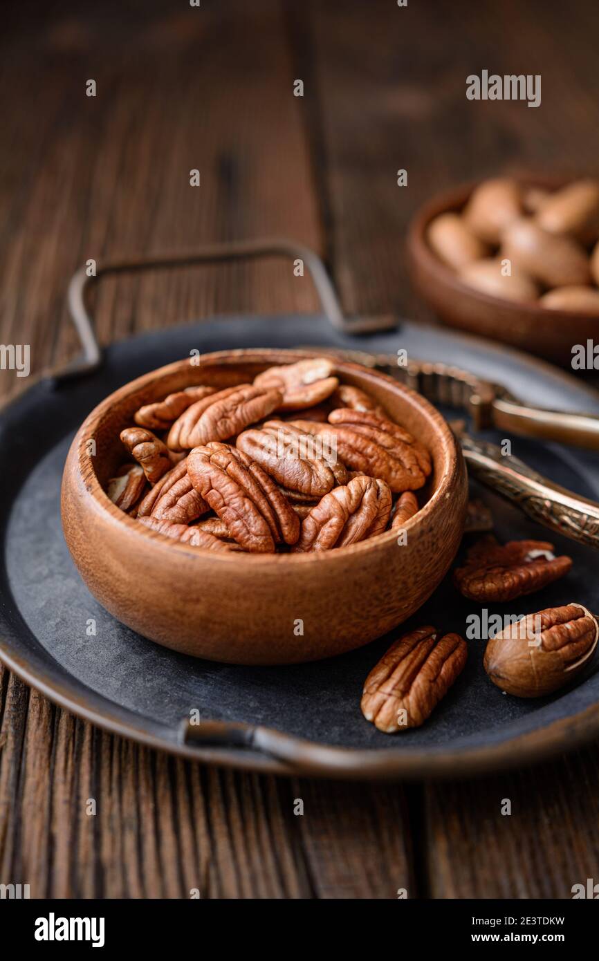 Healthy snack rich in vitamins and minerals, fresh shelled and in-shell pecans in a bowl on wooden background Stock Photo