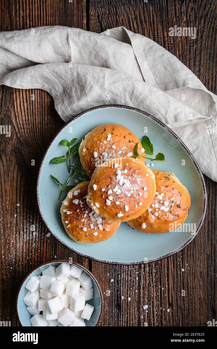 Bath buns, classic English sweet pastry glazed with syrup, topped with caraway seeds and crushed sugar cubes on rustic wooden background Stock Photo